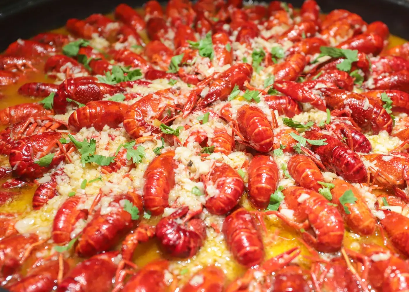 Tray of boiled crawfish covered in garlic butter and chopped garlic