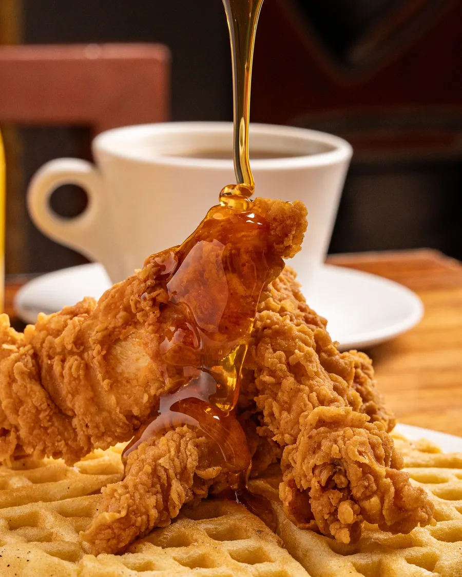 Fried chicken on a waffle with syrup pouring over it