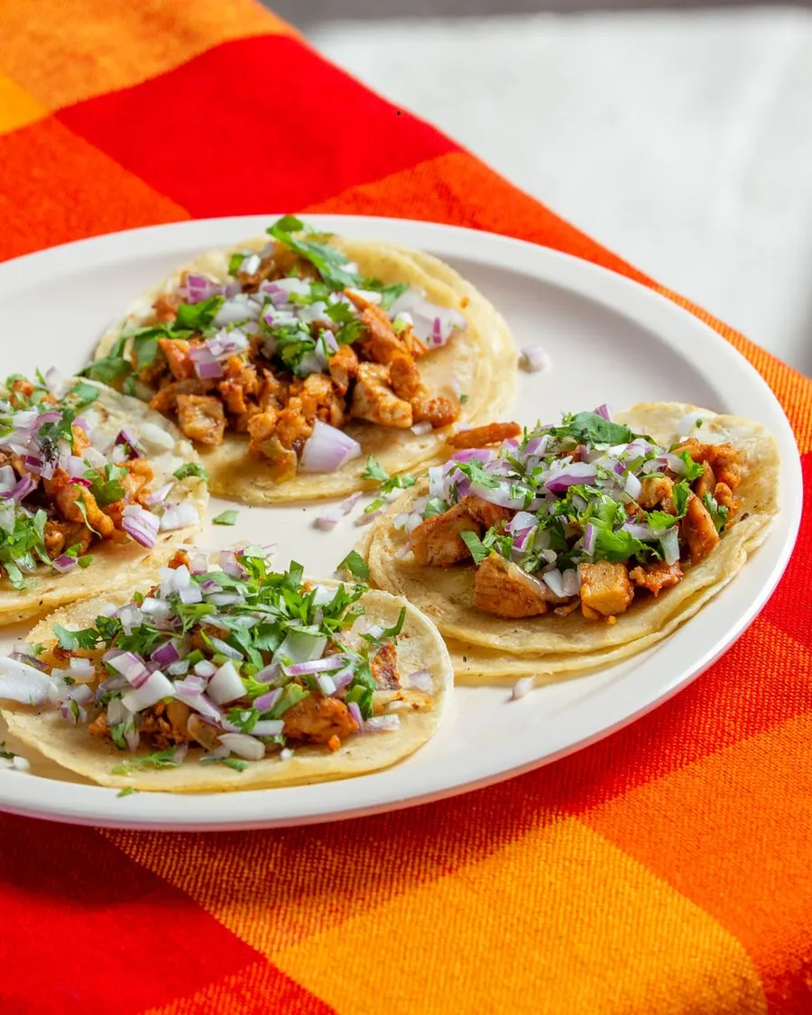 Four street tacos on a white plate